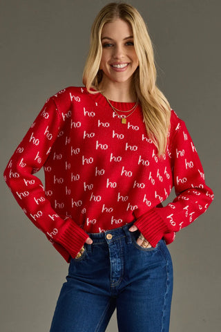Woman wearing a red sweater with 'ho ho ho' pattern and blue jeans on a gray background