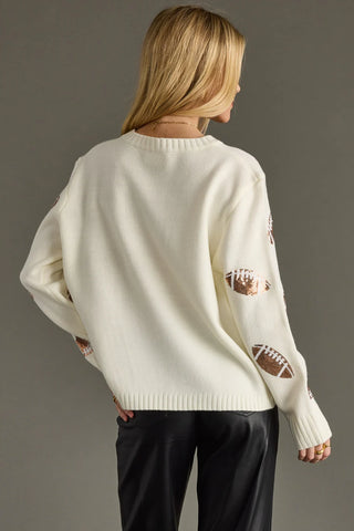Person wearing a cream sweater with football designs on a gray background