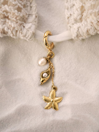Gold earring with starfish and pearl charm on a textured beige background