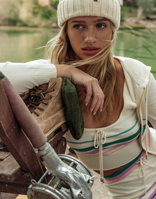 Woman sitting by a lake wearing a striped top and white beanie