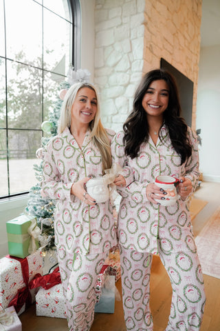 Two women in matching pajamas standing in a festive living room with Christmas decorations.