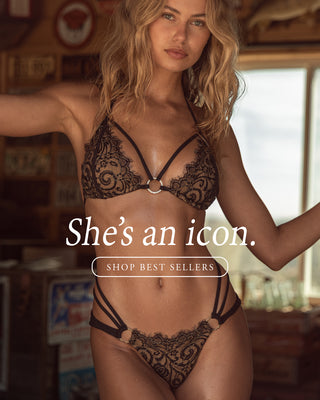 Model wearing a black lace bikini standing by a wooden door. 