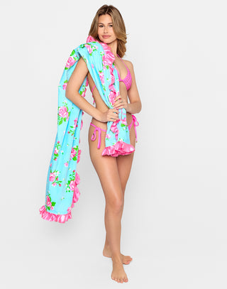 Vintage Rose Towel featuring a bright blue background with an allover pink rose floral print, finished with glossy pink satin ruffle trim and embroidered “Beach Bunny” logo. This romantic, feminine beach towel is perfect for adding a touch of vintage glam to your poolside or beach day.