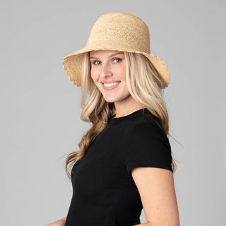 Model wearing a tan crochet bucket hat with a scalloped brim. 